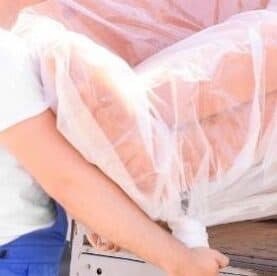 A delivery person holding a wrapped sofa for delivery