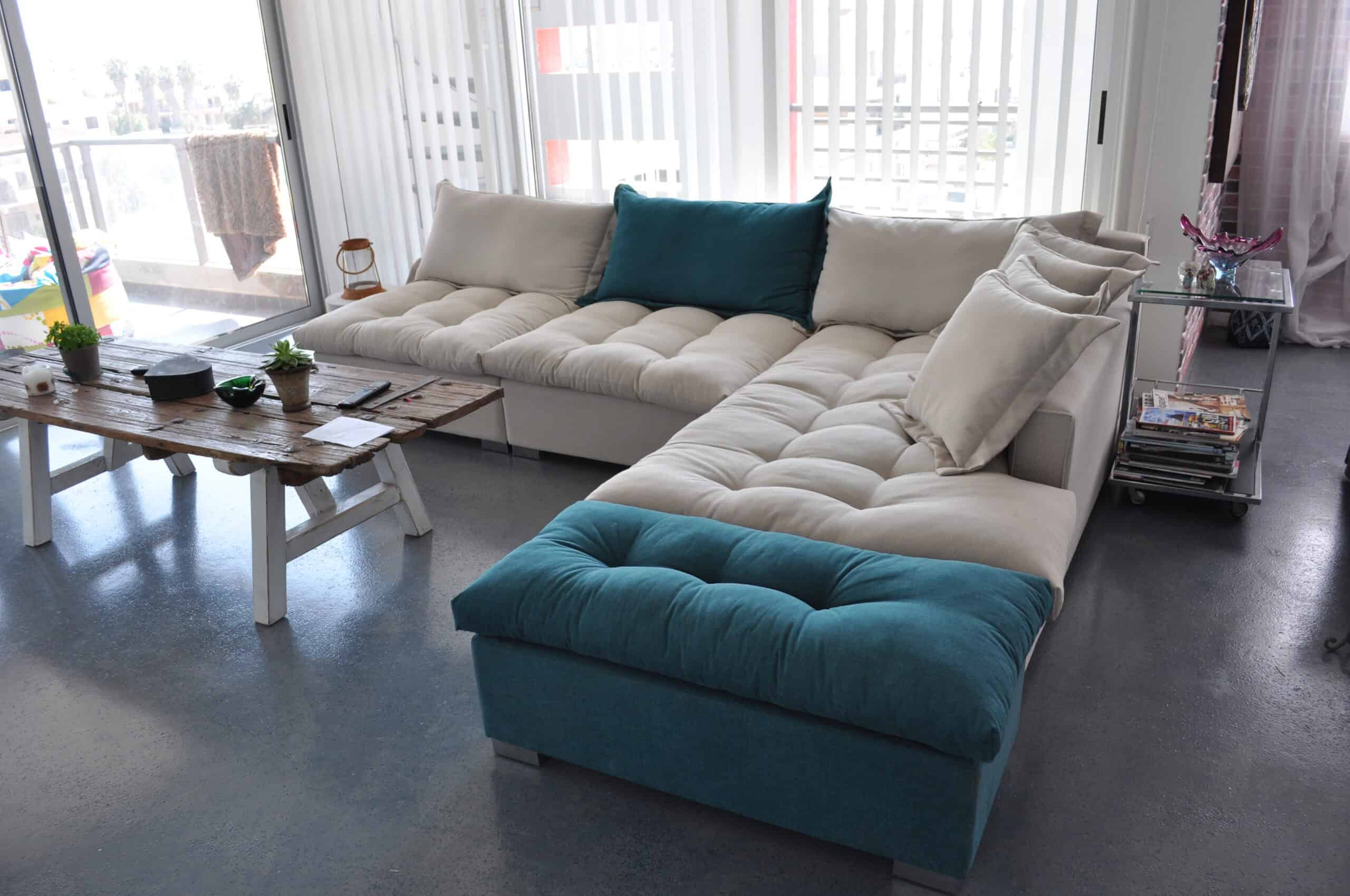 a custom corner sofa in light grey with buttons and removable pouf in petrol colour