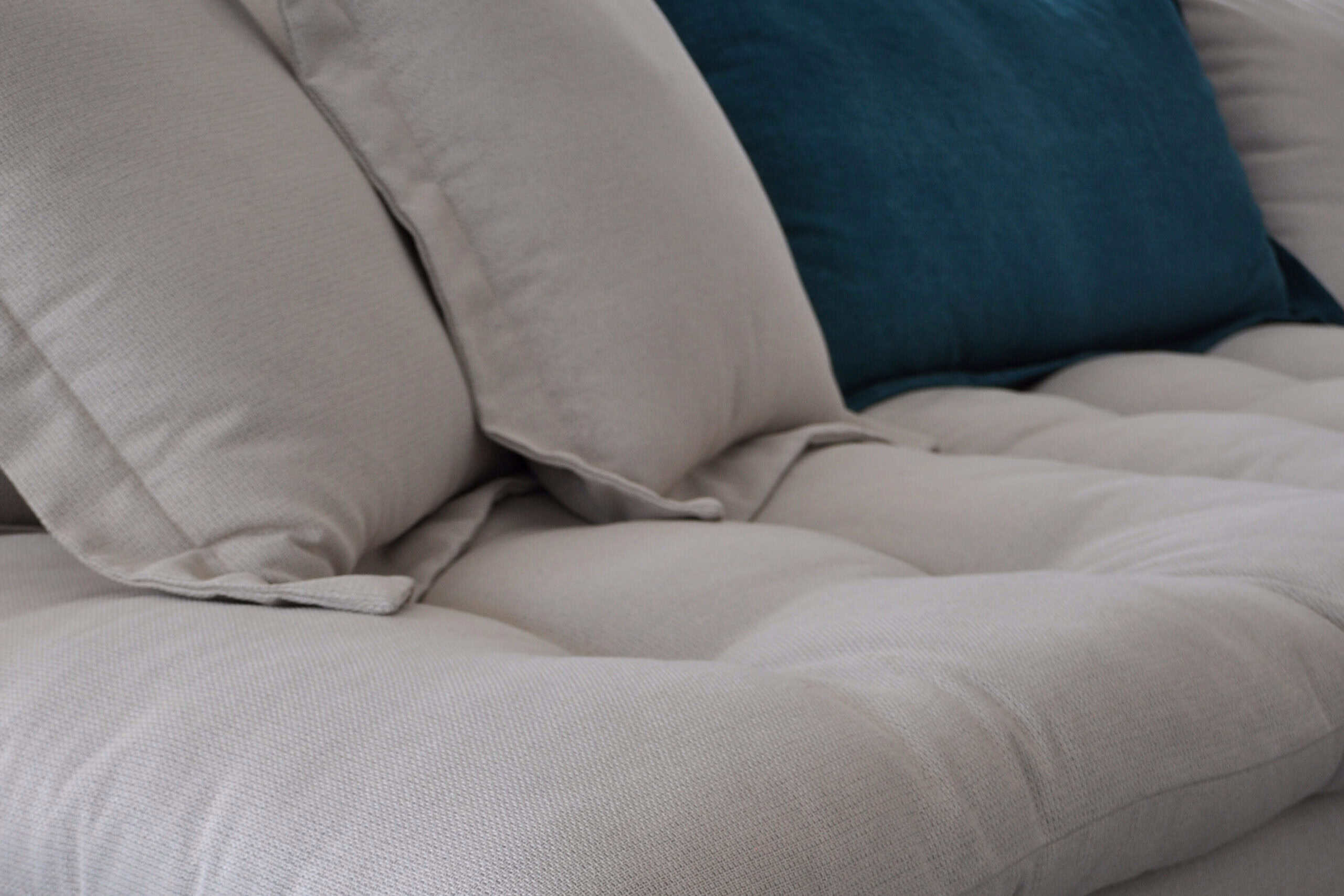 a custom corner sofa in light grey with buttons and removable pouf in petrol colour