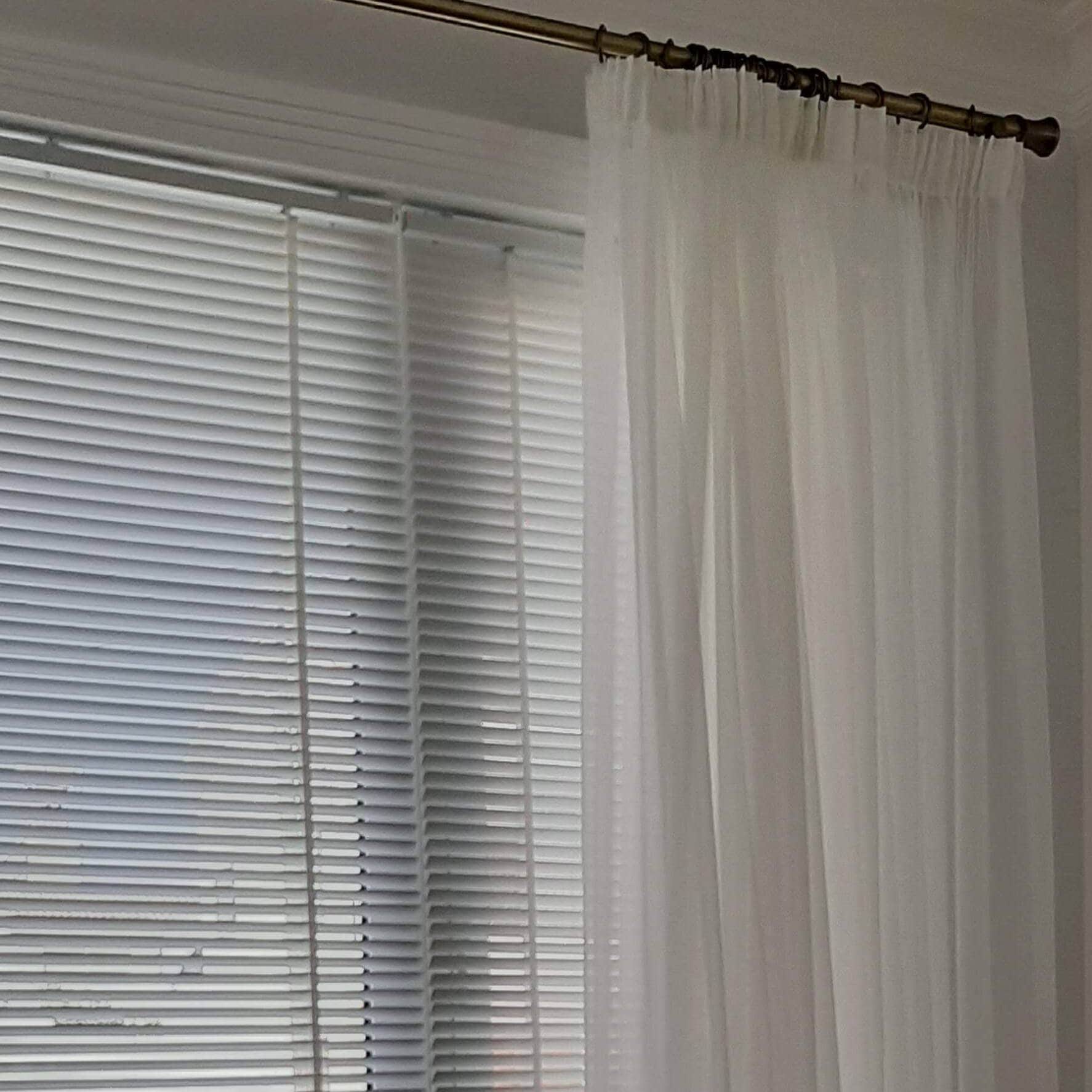 Sheer curtain with a white wooden Venetian blind and an elegant bronze rod